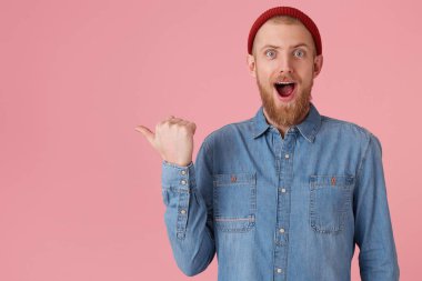Kırmızı kalın sakallı kırmızı şapkalı olumlu duygular memnun adam dolu openes yaygın olarak heyecan, bırakılan çene, ağzına pembe duvar noktaları sol taraftaki kopya alanı için başparmak ile izole dikkat çekiyor