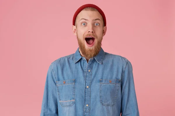 Overflowing with positive emotions glad guy in red hat with red thick beard openes mouth widely in excitement, dropped jaw, isolated on pink wall — Stock Photo, Image