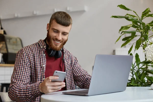 Happy young attractive ginger bearded man working at a laptop wh