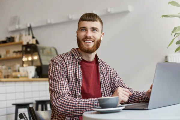 Photo of attractive ginger bearded man working at a laptop, sitt