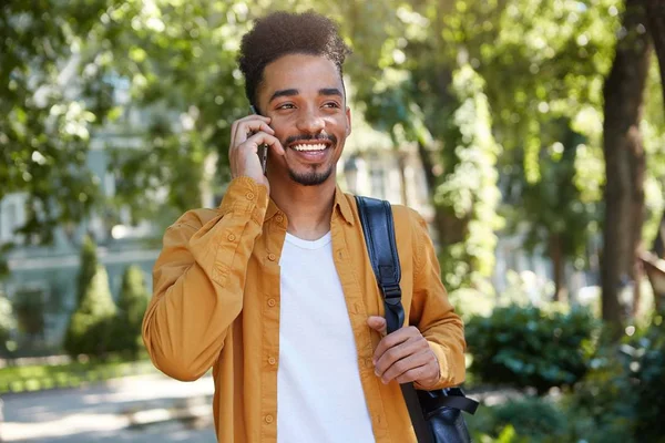 Jeune homme à la peau foncée positive en chemise jaune, marchant au — Photo