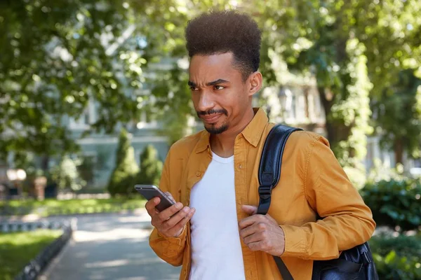 Jeune homme à la peau foncée insatisfaite, bavardant au téléphone avec — Photo