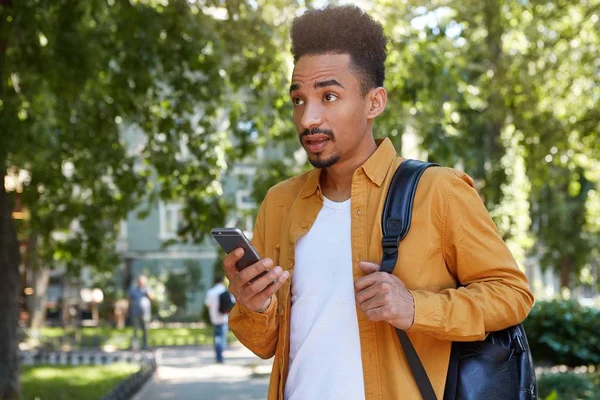 Photo de jeune homme à la peau foncée étonné en chemise jaune marchant un — Photo