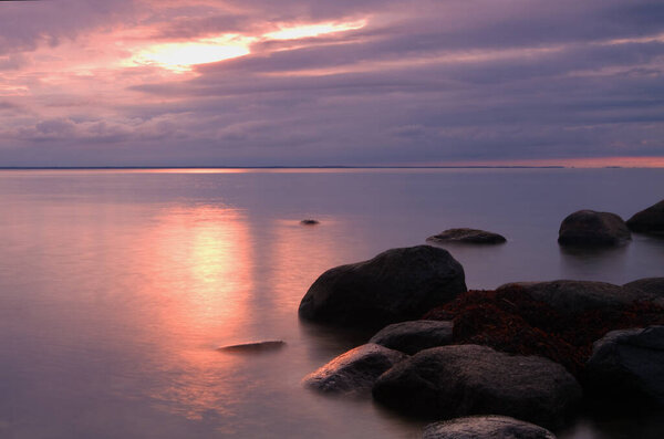 Закат над Балтийским морем после летнего дня, солнце в сиянии сквозь облака