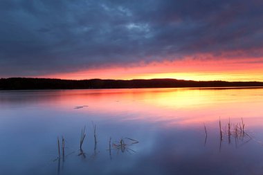 Sakin bir İsveç gölünün üzerinde güzel renkli bir gün batımı