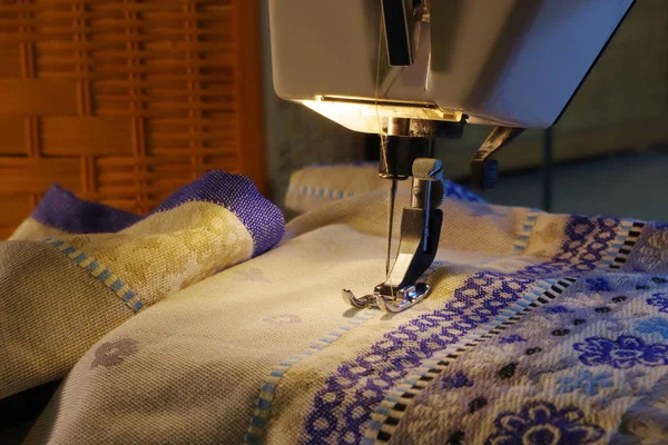 Foot and needle of a sewing machine that is stitching a beige fabric