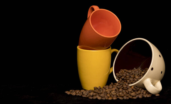Coffee beans spread around coffee mugs on a black background