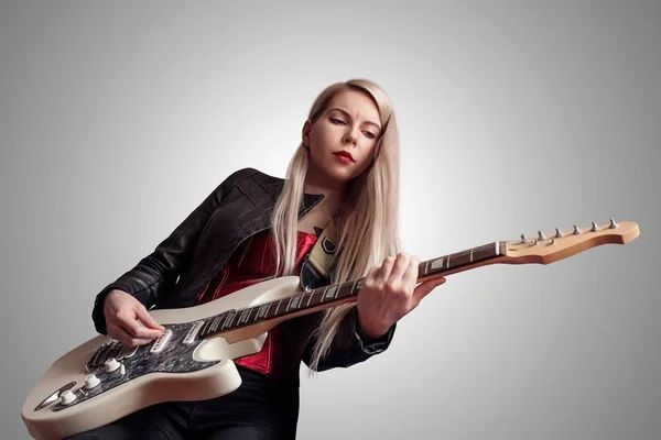 Silver haired woman with pale skin playing electric guitar on grey background.