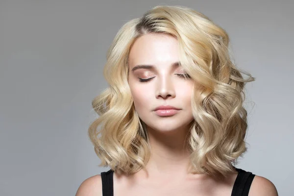 Gri bir arka plan, doğal makyaj ve temiz bir cilt üzerinde bukleler ile Blonde. güzel bir gülümseme, gözleri kapalı. Portre 