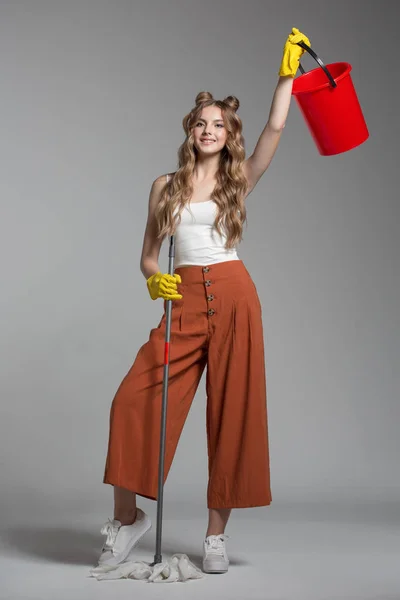 La donna alla moda con capelli lunghi tiene in mano un secchio rosso e uno straccio Fotografia Stock