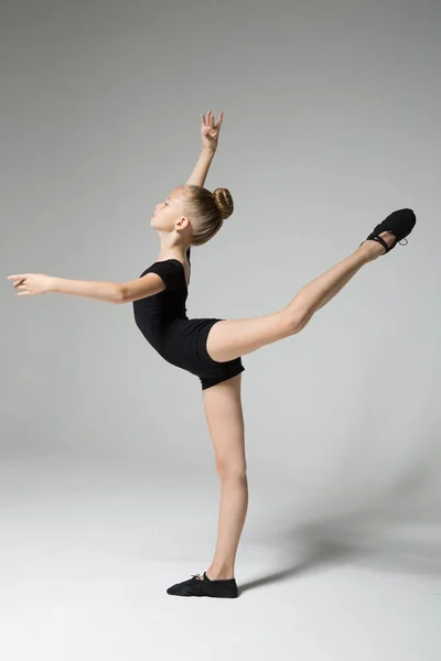 Uma bailarina em roupas pretas faz uma pose "Engolir". Jovem menina flexível . Imagem De Stock