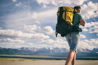 Adam sırtında bir sırt çantası ile bir asfalt yol boyunca yürüyor