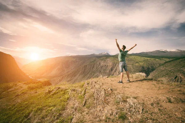 Um homem com uma mochila no topo de uma montanha. Levantando as mãos e desfrutando do nascer do sol no vale Imagens Royalty-Free