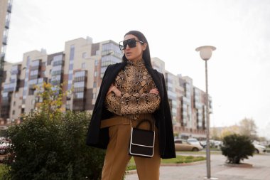 Güneş gözlüklü ve takım elbiseli moda kadını. Şehirde dikiliyor.
