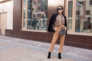 Güneş gözlüklü ve takım elbiseli moda kadını. Şehirde dikiliyor.