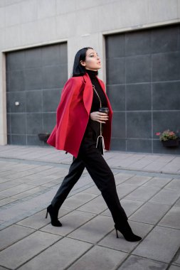 Kırmızı paltolu moda kadını şehirde dolaşıyor. Bir fincan kahve.