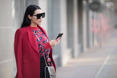 Kırmızı ceketli bir iş kadını telefonda konuşuyor. Akıllı telefon içeri. 