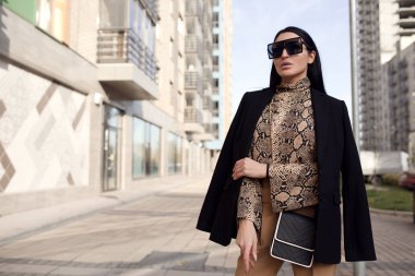 Güneş gözlüklü ve takım elbiseli moda kadını. Şehirde dikiliyor.