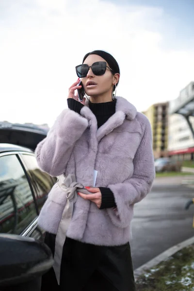 Moda kadını telefonda konuşuyor. Arabanın yanında duruyor. Cam.