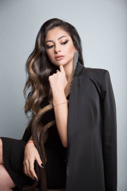 Uzun kıvırcık saçlı güzel esmer bir sandalyede oturuyor. Evet.