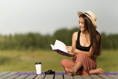Gülümseyen mutlu genç kadın bir kitap okuyor. Kız parkta dinleniyor. Kopyala