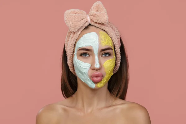 woman cleansing facial mask. Clay of blue-yellow cream covers part of the face. home headband. blow a kiss