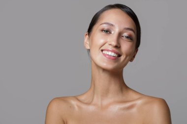 Temiz tenli güzel bir esmer. Yüz ve vücut bakımı. Gri arkaplan