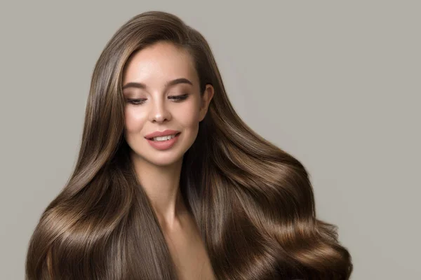 Dalgalı saçlı, gülümseyen esmer bir kadının portresi. Gri arka planda saç stili ve makyajı olan kadın.