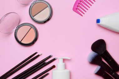 Pudralı allık, aplikatörlü konteynır ve pembe arka planda makyaj fırçaları. Makyaj seti