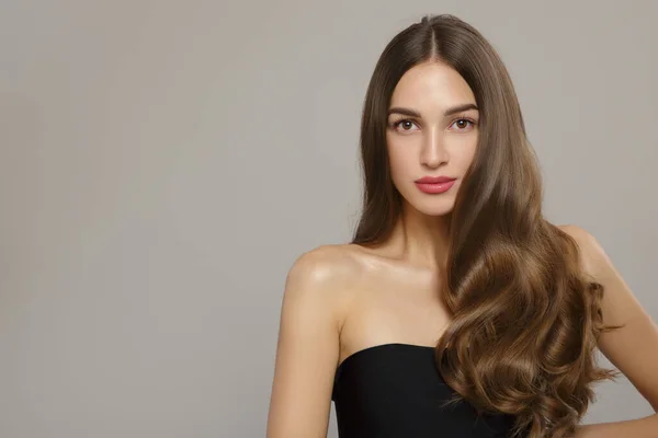 Dalgalı saçlı ve makyajlı güzel bir kadın. Gri bir arkaplanda