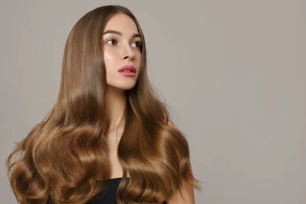 Dalgalı saçlı ve makyajlı güzel bir kadın. Gri bir arkaplanda
