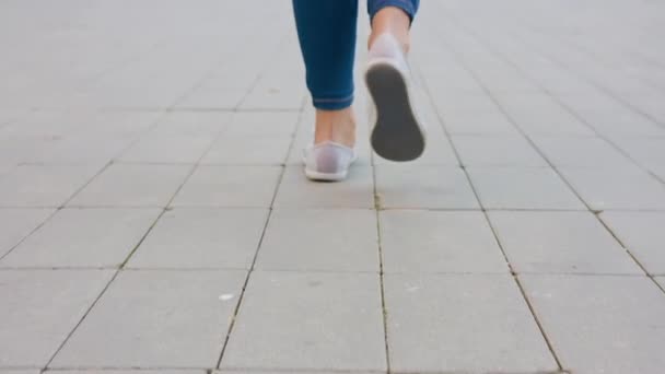 タイル張りの舗装を歩く若い女性の低角度ハンドヘルドショット. — ストック動画