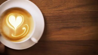 Elinizde beyaz bir bardak kapuçino ve ahşap masada zarif bir latte tablosu var. Kahve dükkanı markaları, menüler, bloglar veya yaşam tarzı içeriği için ideal.