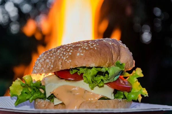 Hambúrguer saboroso e insalubre clássico na frente da chama de fogo. Ganhar peso comida de rua e fast food. — Fotografia de Stock