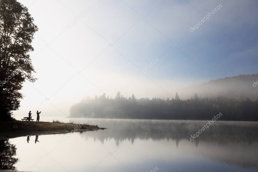 Foggy river in morning with fishermen silhouettes