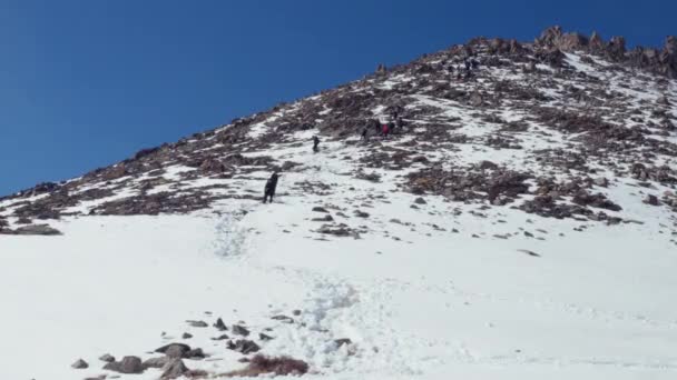 Tired climbers descend from a rocky mountain along snow-covered path. Winter day — Stock Video