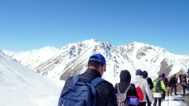 Excursionistas en las montañas de invierno que van a subir la cima de una colina rocosa. disparado por detrás — Vídeo de stock