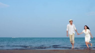 Balayı yeni evli genç çift sahilde el ele tutuşarak aşk yürüyor