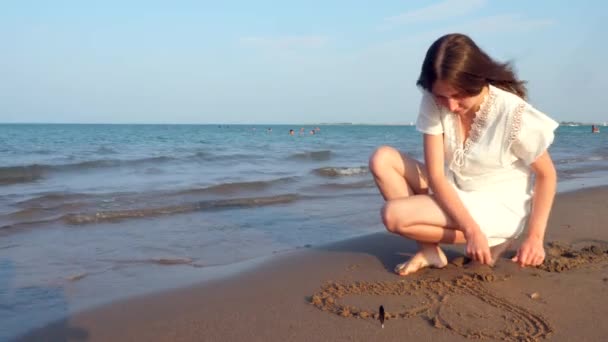 Menina adolescente solitária desenha um coração na areia — Vídeo de Stock