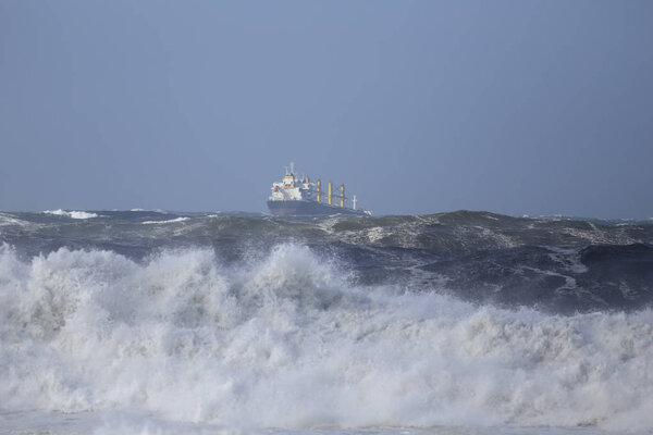Commercial ship sailing under storm in the sea with big waves but with a beautiful blue sky