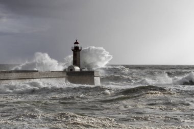 Huysuz deniz dalgaları iskele ve eski deniz feneri karşı girmesini büyük sıçrama ile. Gün ışığı sonu. Nehir Douro ağzı, Porto, Portekiz.