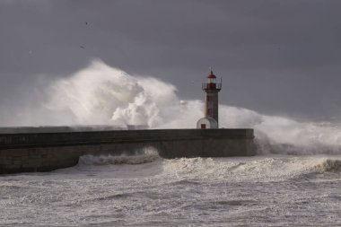 Fırtınalı karanlık bulutlu gökyüzüne karşı büyük beyaz dalgalar ve deniz feneri. Douro nehri ağzı, Porto, Portekiz.
