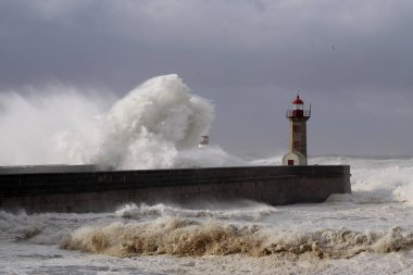 Fırtınalı karanlık bulutlu gökyüzüne karşı büyük beyaz dalgalar ve deniz feneri. Douro nehri ağzı, Porto, Portekiz.