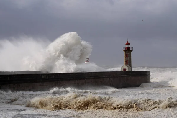 Big white waves over piers and lighthouse against a stormy dark cloudy sky. Douro river mouth, Porto, Portugal.