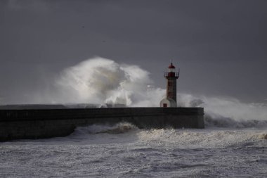 Fırtınalı karanlık bulutlu gökyüzüne karşı büyük beyaz dalgalar ve deniz feneri. Douro nehri ağzı, Porto, Portekiz.