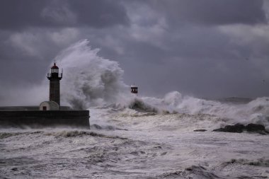 Fırtınalı karanlık bulutlu gökyüzüne karşı büyük beyaz dalgalar ve deniz feneri. Douro nehri ağzı, Porto, Portekiz.