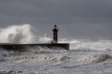Fırtınalı karanlık bulutlu gökyüzüne karşı büyük beyaz dalgalar ve deniz feneri. Douro nehri ağzı, Porto, Portekiz.