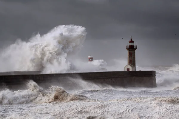 Big white waves over piers and lighthouse against a stormy dark cloudy sky. Douro river mouth, Porto, Portugal.