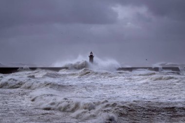 Fırtınalı karanlık bulutlu gökyüzüne karşı büyük beyaz dalgalar ve deniz feneri. Douro nehri ağzı, Porto, Portekiz.
