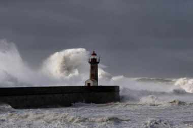Rıhtımlar üzerinde büyük beyaz dalgalar ve deniz feneri yağmurdan önce kara bulutlu bir gökyüzüne karşı. Douro nehri ağzı, Porto, Portekiz, deniz fırtınası sırasında.